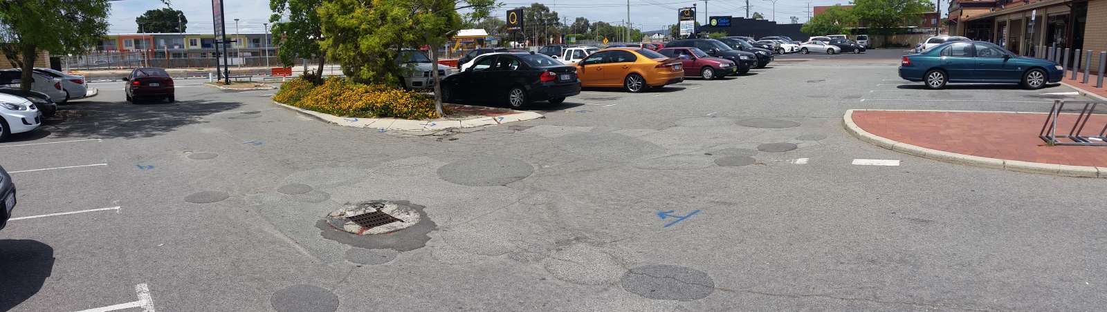 Damaged asphalt car park at Hambleys IGA and Tavern in Queens Park with damaged soakwell and potholes which have been patched over.